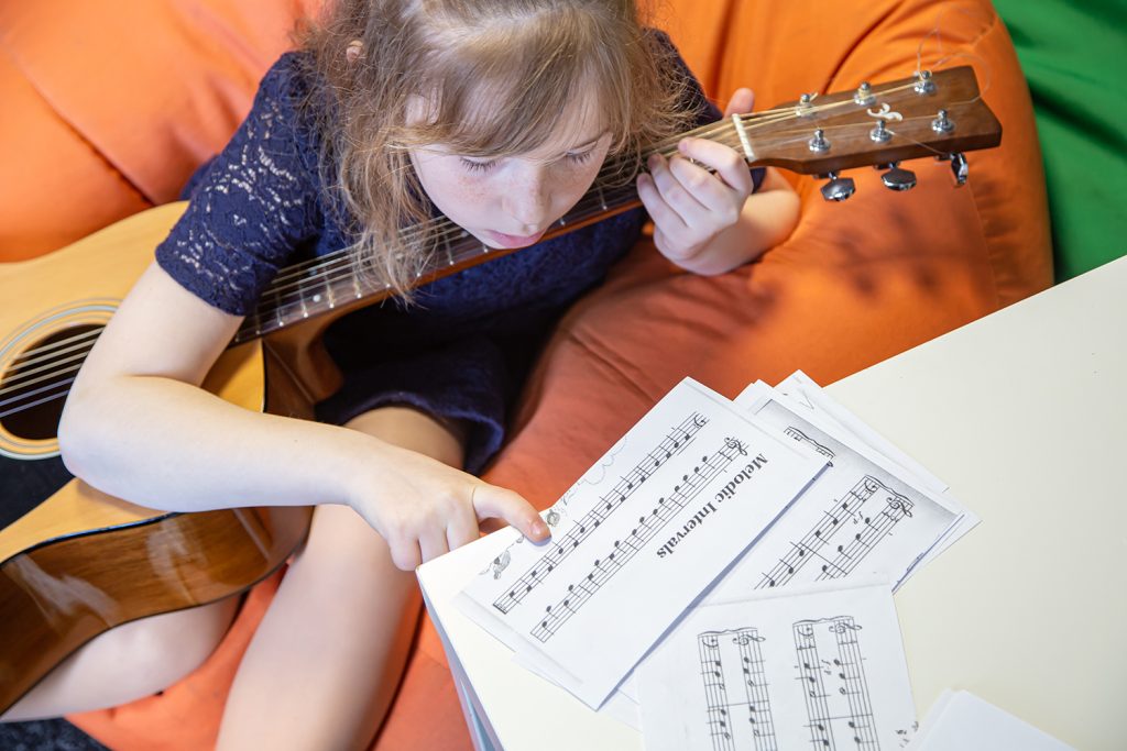 Niña mirando partitura para aprender a tocar la guitarra
